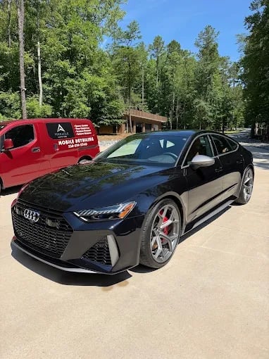Black Audi sedan with red accents parked in front of a red truck and wooded area