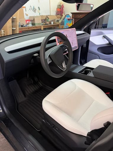 Modern car interior with gray steering wheel, white and black seats, and dashboard visible through open door in garage setting