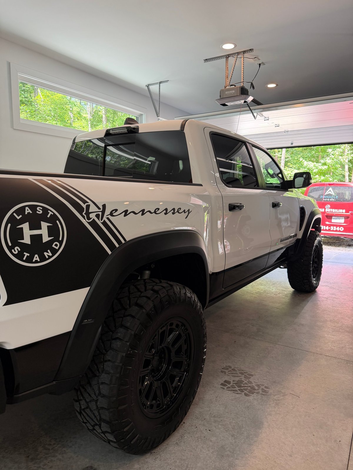 White and black lifted pickup truck with Hennessey branding displayed in an indoor showroom with large windows