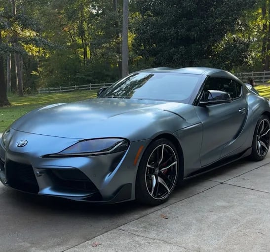 Silver Toyota Supra sports car parked on a driveway with trees in the background