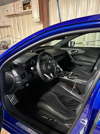 Interior view of a blue sports car with black leather seats, steering wheel, and dashboard visible through the open door