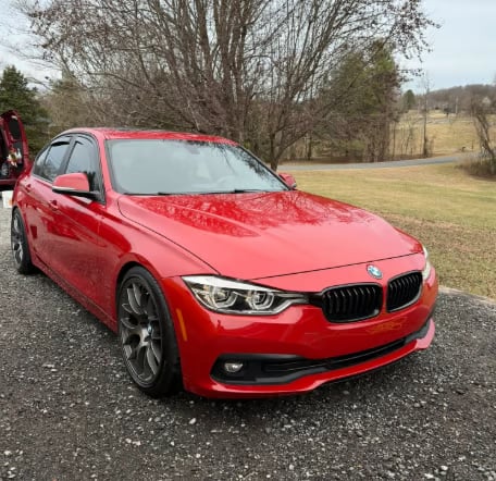 Red BMW sedan parked on a driveway with bare trees and grassy field in the background